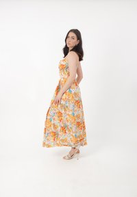 Maxi kjole med blomstermønster i orange og blå nuancer, med en tætsiddende bodice, spaghetti-stropper og flydende nederdel. Båret med hæle.