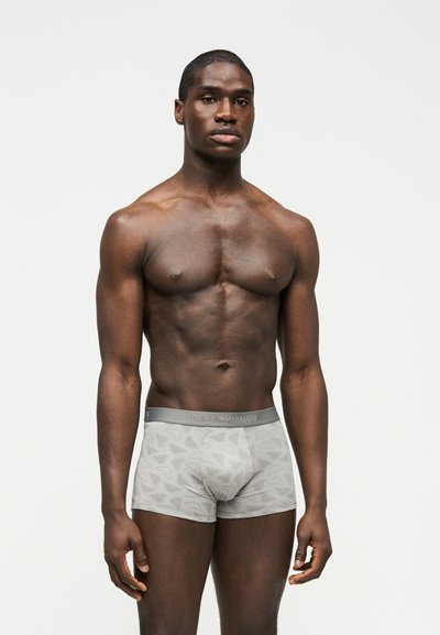 Lihaseline mees seisab näoga ettepoole, kannab halli Emporio Armani bokserpüksteid, millel on peen logo muster, tavalise valge tausta ees.