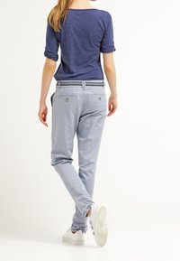 Jasnoniebieskie spodnie o dopasowanym kroju z ciemnym paskiem wzdłuż pasa, zestawione z ciemnoniebieską bluzką z podwiniętymi rękawami i białymi trampkami.