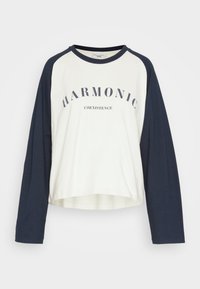 Weißes und marineblaues Langarm-T-Shirt mit abgerundetem Saum, Rundhalsausschnitt und dem Text "HARMONIC COEXISTENCE" auf der Vorderseite.