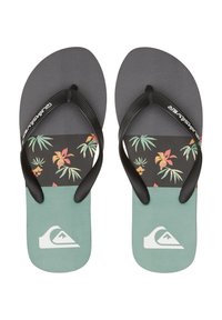 Flip-flopit musta mustalla hihnalla, joissa on trooppisia lehtiä vihreinä, oransseina ja beigeinä mustalla taustalla, ja mintunvihreä pohja.