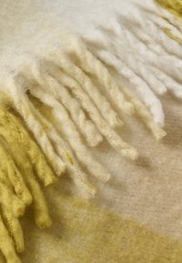 Blød uldent stof med frynseender i nuancer af creme, beige og gul, der viser detaljeret tekstur og fibre.