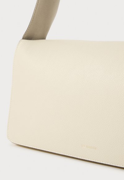 Borsa a spalla in pelle crema con una texture liscia, dotata di una tracolla grigia e un discreto marchio in rilievo nell'angolo inferiore.