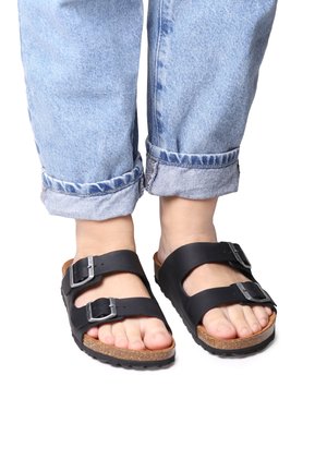 Sandali neri in pelle con due fibbie regolabili, soletta in sughero e suola in gomma. Indossati con jeans blu arrotolati.