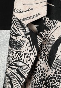 Gros plan d'un tissu avec des motifs floraux abstraits noirs et beiges ainsi que des motifs à pois sur un matériau plié.