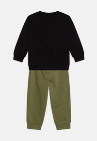 Conjunto de dos piezas que incluye una parte superior de manga larga negra con un cierre de botón en la parte posterior y pantalones de chándal verdes con puños y cinturilla elástica.