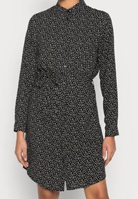 Abito nero con bottoni, decorato con pois bianchi, maniche lunghe e vita cinturata. Tessuto liscio con una vestibilità leggermente rilassata e orlo arrotondato.