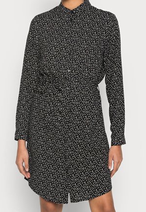 Schwarzes Hemdkleid mit weißen Polka-Dots, langen Ärmeln und tailliertem Gürtel. Glatte Stoffqualität mit einem leicht lockeren Schnitt und abgerundetem Saum.