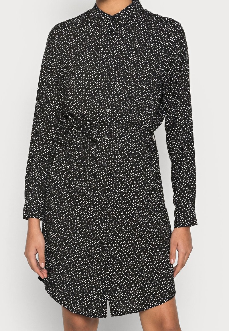 Abito nero con bottoni, decorato con pois bianchi, maniche lunghe e vita cinturata. Tessuto liscio con una vestibilità leggermente rilassata e orlo arrotondato.