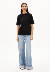 Zwarte t-shirt met korte mouwen, gecombineerd met lichtblauwe, hoge taille, wijde jeans, met een opgevouwen zoom en lichte stikdetails.