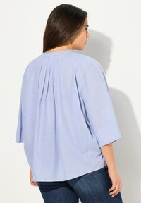 Blusa azzurro chiaro realizzata in un morbido tessuto testurizzato, con un taglio rilassato, maniche ampie e pieghe posteriori per un tocco di dettaglio in più.