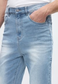 Ljusblå denimjeans med en lätt sliten textur. Har knappstängning, framfickor och klassisk raka ben.