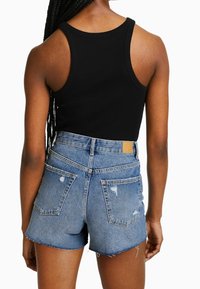 Svart ribbad linne som kombineras med högmidjade, slitna blå denimshorts. Har fransad fåll och två bakfickor.