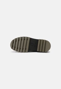 Suela de zapato negra con textura estriada, hecha de goma. Presenta una punta redonda y un tacón plano. Logo impreso cerca del tacón. Color: oscuro con acentos en gris claro.