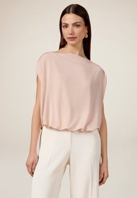 Top in morbido tessuto di un rosa chiaro, con una vestibilità ampia e maniche corte, caratterizzato da un collo rotondo. Abbinato a pantaloni bianchi a vita alta.