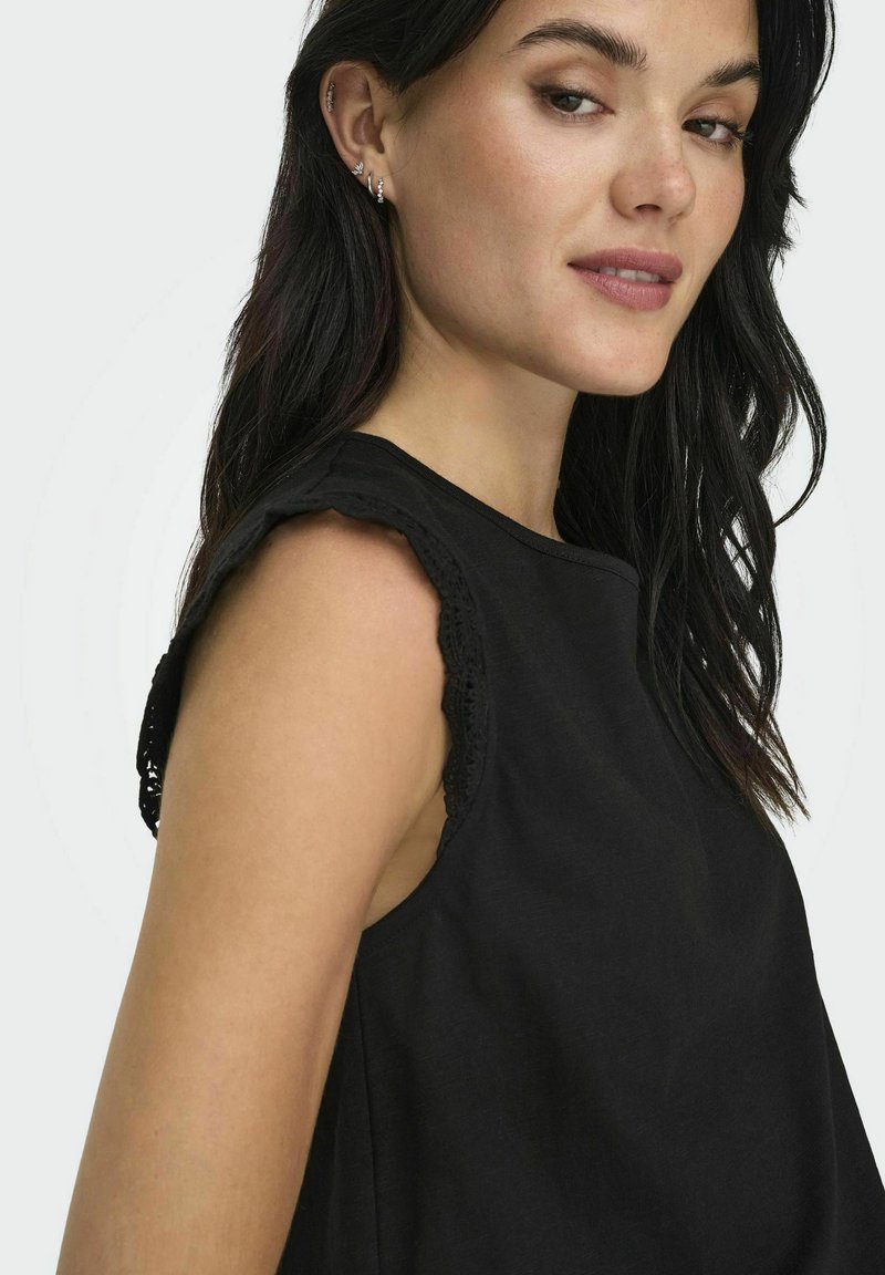 Haut sans manches noir avec une finition en dentelle à ourlet sur les épaules, en coton, coupe décontractée et encolure ronde, affichant une texture lisse.