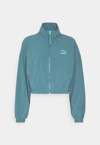 Kort turkis jakke lavet af letvægtsstof, med høj krave, lynlåslukning og elastiske kanter ved ærmer og bund. Puma-logo på brystet.
