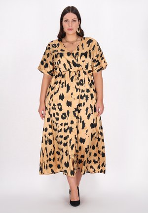 Beige leopardmønstret maxikjole med indpakningsdesign, korte ærmer, en indsnøret talje og en glat, skinnende tekstur. Sorte højhælede sko bemærket.