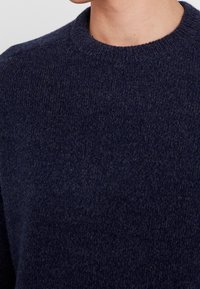 Maglione girocollo in lana navy con una finitura texture, caratterizzato da un colletto a coste e un tessuto morbido, che presenta un design classico e minimalista.