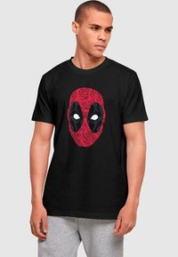 Camiseta de algodón negra con un diseño de la máscara de Deadpool en rojo, rodeada de patrones de rosas, con detalles en negro y ojos blancos.