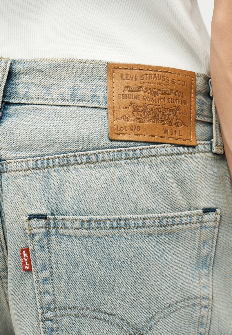 Hellblaue Jeans aus Denim mit Lederetikett der Marke Levi's und rotem Levi's-Tag auf der Gesäßtasche, getragen mit weißem, geripptem Shirt.