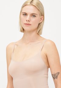 Lightweight, nude-colored camisole with adjustable straps, a smooth texture, and a fitted design. No visible seams or embellishments.
