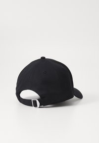 Mustapohjainen beanie, jossa on kaareva lippa ja joka on valmistettu puuvillatwiilistä. Takana on säädettävä hihna ja päällä nappi.