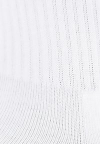 Biała dzianina z pionowymi prążkami, gładka w dotyku, o lekko podniesionej, miękkiej strukturze.