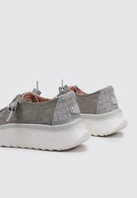 Zapatillas deportivas grises con parte superior de tela texturizada, forro interior acolchado y suela gruesa blanca moteada. Incluyen cordones ajustables y detalle del logo.