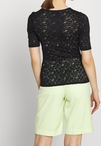 Svart spetsblus med korta ärmar som har ett blommönster, i kombination med ljusgröna shorts. Tyget har en genomskinlig textur.