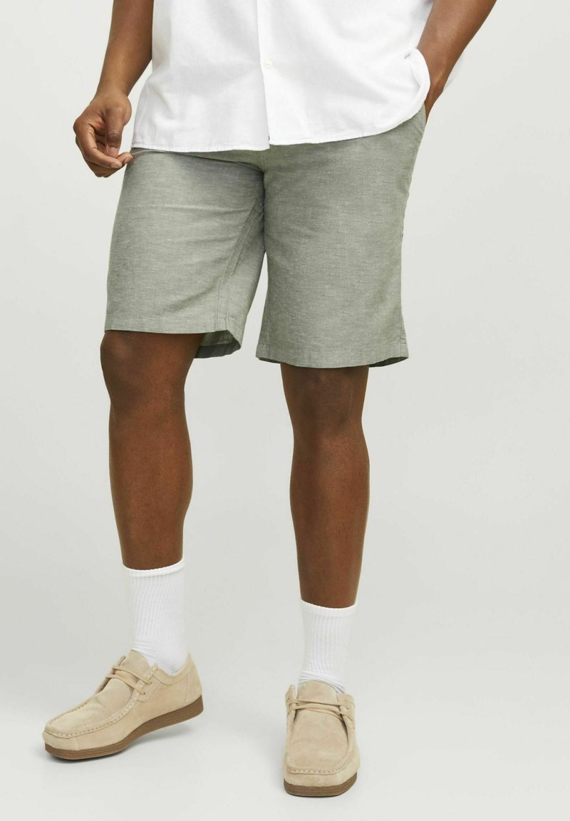 Hellegraue Leinenshorts mit lockerer Passform, etwas oberhalb des Knies, kombiniert mit beigen Schuhen und weißen Socken.