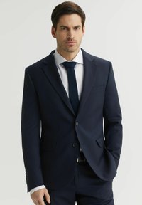 Granatowa marynarka o eleganckim kroju, z dwoma przednimi kieszeniami i zapięciem na jeden guzik, zestawiona z białą koszulą i ciemnym krawatem.