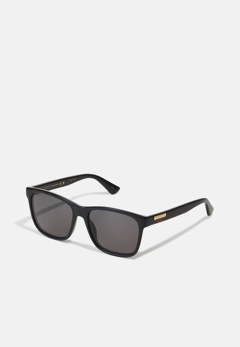 Gafas de sol negras con montura cuadrada, lentes grises y detalle del logo en dorado en las patillas. Fabricadas en plástico con textura suave.