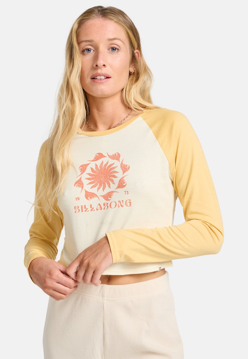 Langemouwen cropped top in crème en geel. Heeft een centrale grafiek in oranje, met ribbeltextuur en contrasterende mouwkleur.