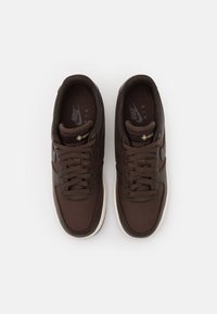 Zapatillas Nike Air en tela marrón oscuro con acentos texturizados, con una suela de goma blanca y un sistema de cordones destacado.