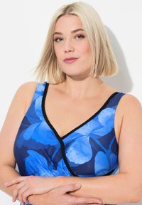 Maillot de bain floral bleu avec un décolleté en V profond et une bordure noire contrastante. Le tissu est lisse avec une finition brillante et un design enroulé.