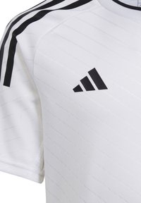 Maglia atletica bianca con strisce nere sulle spalle, realizzata in tessuto testurizzato, con logo Adidas nero sul petto.