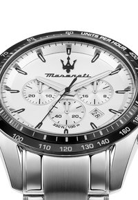 Silverfärgad klocka i rostfritt stål med en vit urtavla, tre subdials, svart bezel och Maserati-logotyp. Vattentålig upp till 100 meter.