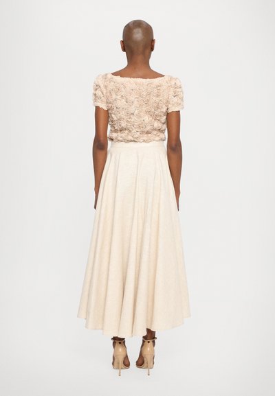 Blomstrete beige topp med korte ermer, sammen med en flytende kremfarget skjørt som går til ankelen og nøytrale høyhælte sko.