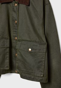 Giacca verde oliva con grandi tasche a patta fissate da bottoni a pressione in ottone e colletto in velluto a coste marrone.