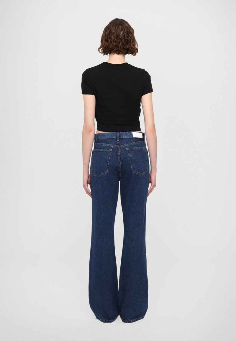 Dunkelblaue, weit geschnittene Jeans mit hoher Taille, die fünf Taschen und eine klassische Denim-Textur aufweisen. Darüber ein eng anliegendes schwarzes T-Shirt.