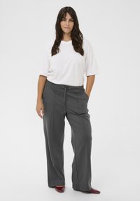 Grijze wijde broek met een trekkoord in de taille, gecombineerd met een eenvoudig wit T-shirt met korte mouwen. Glad textuur; minimale details.