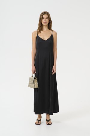 Maxi abito nero con spalline sottili, texture liscia e scollatura a V, abbinato a una piccola borsa con motivo in pelle di serpente e infradito nere.