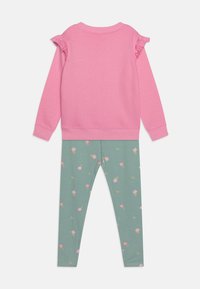Felpa rosa con dettagli a volant sulle spalle, abbinata a leggings verdi con motivi floreali rosa. Tessuto morbido, vestibilità rilassata.
