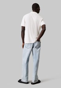 Witte polo met korte mouwen met een gestructureerde afwerking, gecombineerd met lichtblauwe recht geplooide jeans en zwarte instap sandalen.