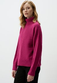 Pull fuchsia avec un col monté côtelé, des manches longues et une texture douce. Présente un ourlet et des poignets côtelés pour plus de détails.