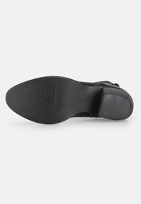 Suela de zapato de cuero negro con una superficie lisa. Presenta un ligero tacón y un logo grabado. Forma general redondeada con bordes texturizados.