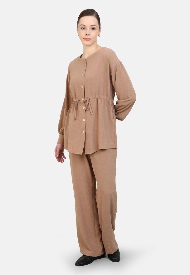 Ensemble bi-matière beige comprenant un haut à boutons avec une taille à cordon de serrage et des manches longues, associé à un pantalon assorti ample.
