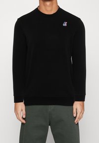 Schwarzer Pullover mit langen Ärmeln, Rundhalsausschnitt und gerippten Bündchen. Verfügt über ein kleines, mehrfarbiges Markenlogo auf der linken Brust.