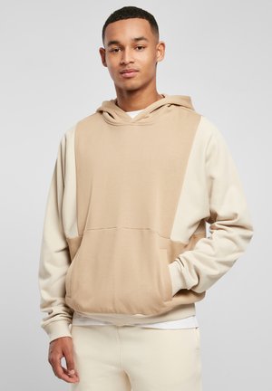 Sweatshirt cu glugă bej și crem, având o buzunar tip kangaroo, croială lejeră și un design cu panouri contrastante. Material moale cu o textură netedă.